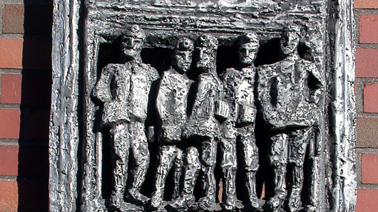 Aluminiumrelief zeigt einen zweietagigen Förderkorb, in dem Bergleute stehen.